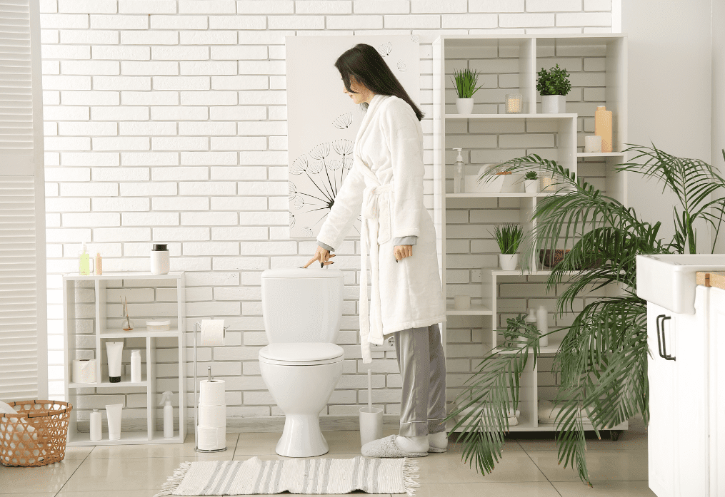 A woman in white robe standing next to toilet.